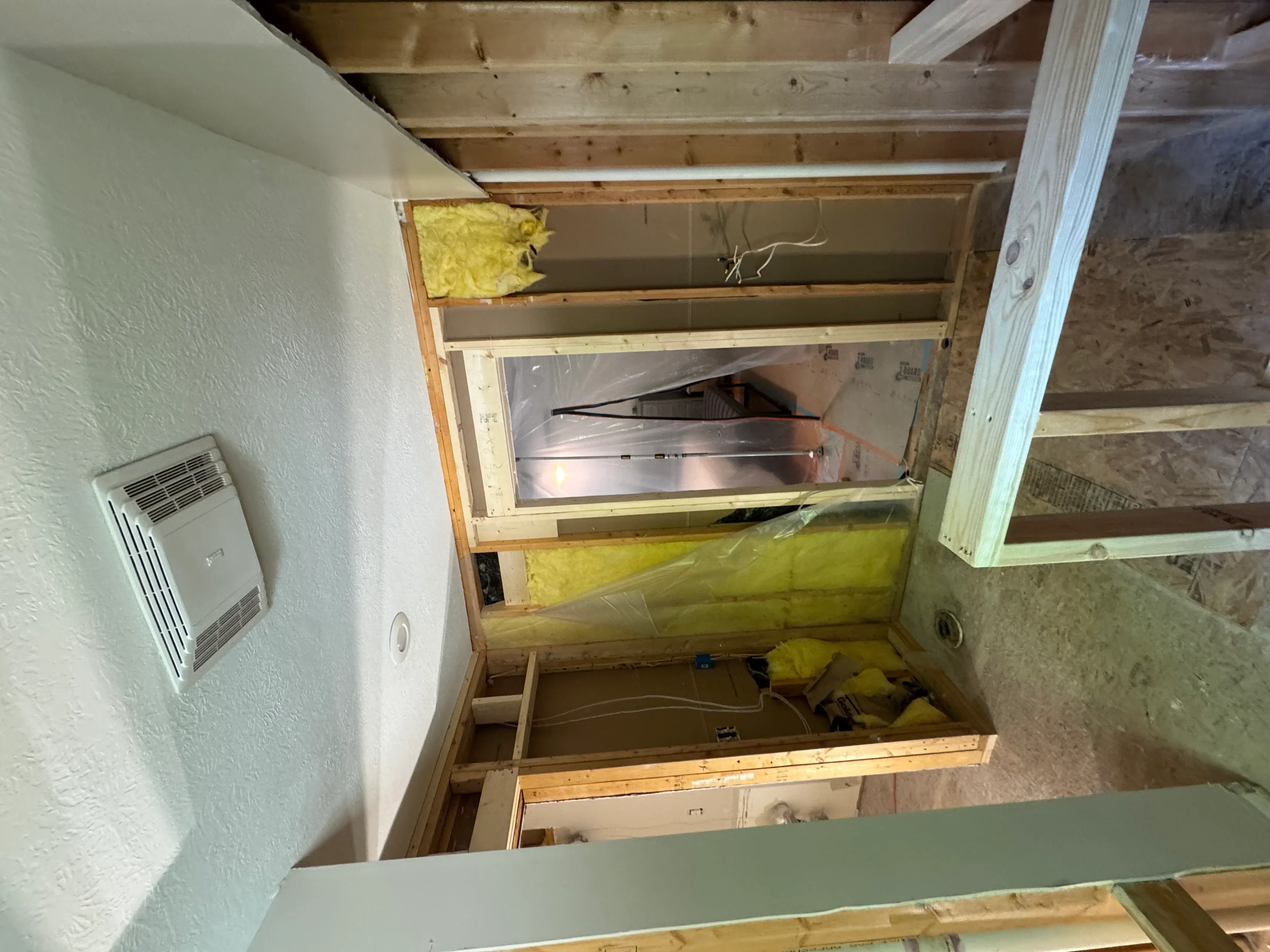 Bathroom exhaust fan installation with metal ductwork, lumber framing, and yellow fiberglass insulation