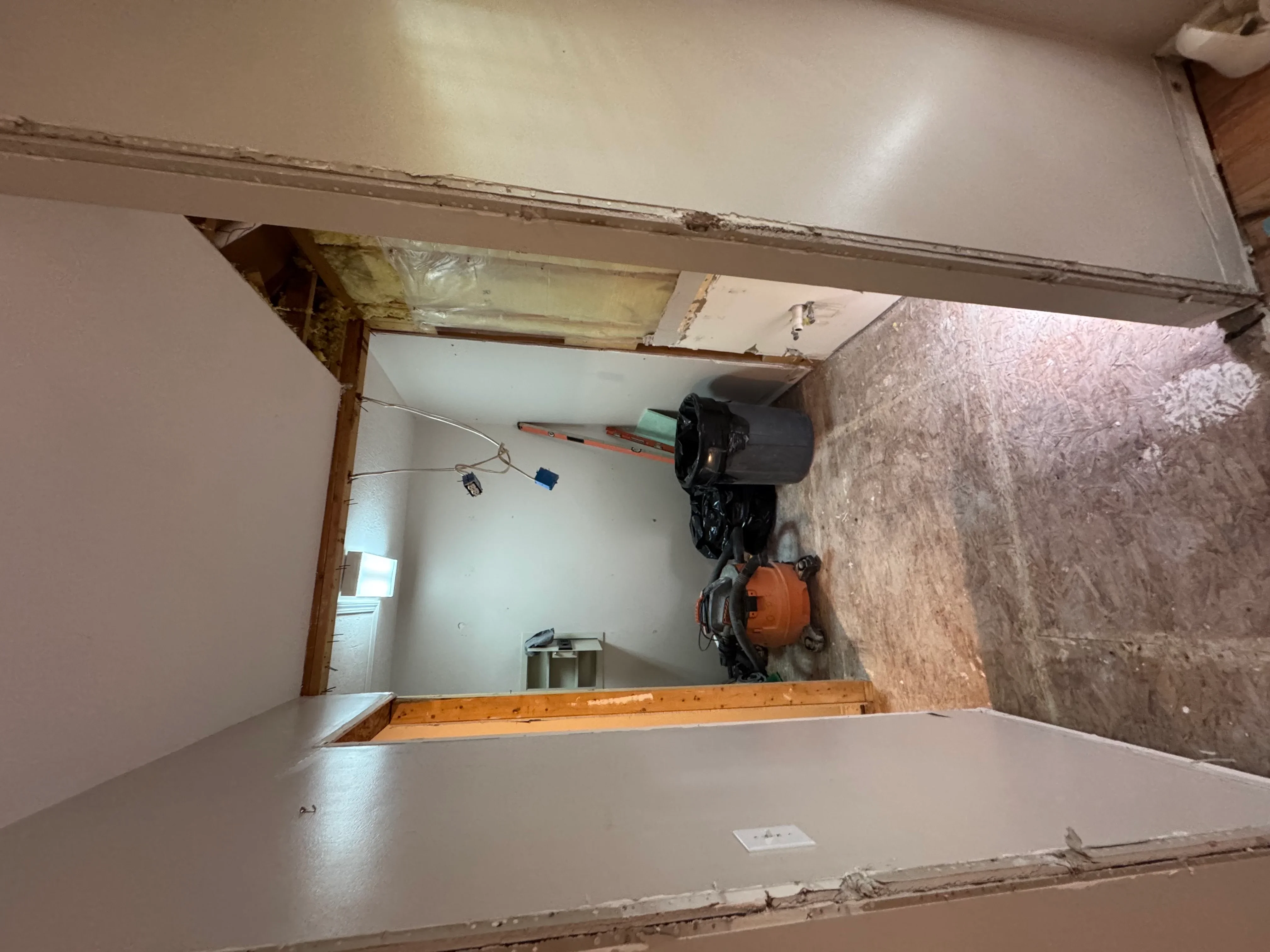 Drywall installation with exposed framing, electrical wiring, and construction materials in interior renovation
