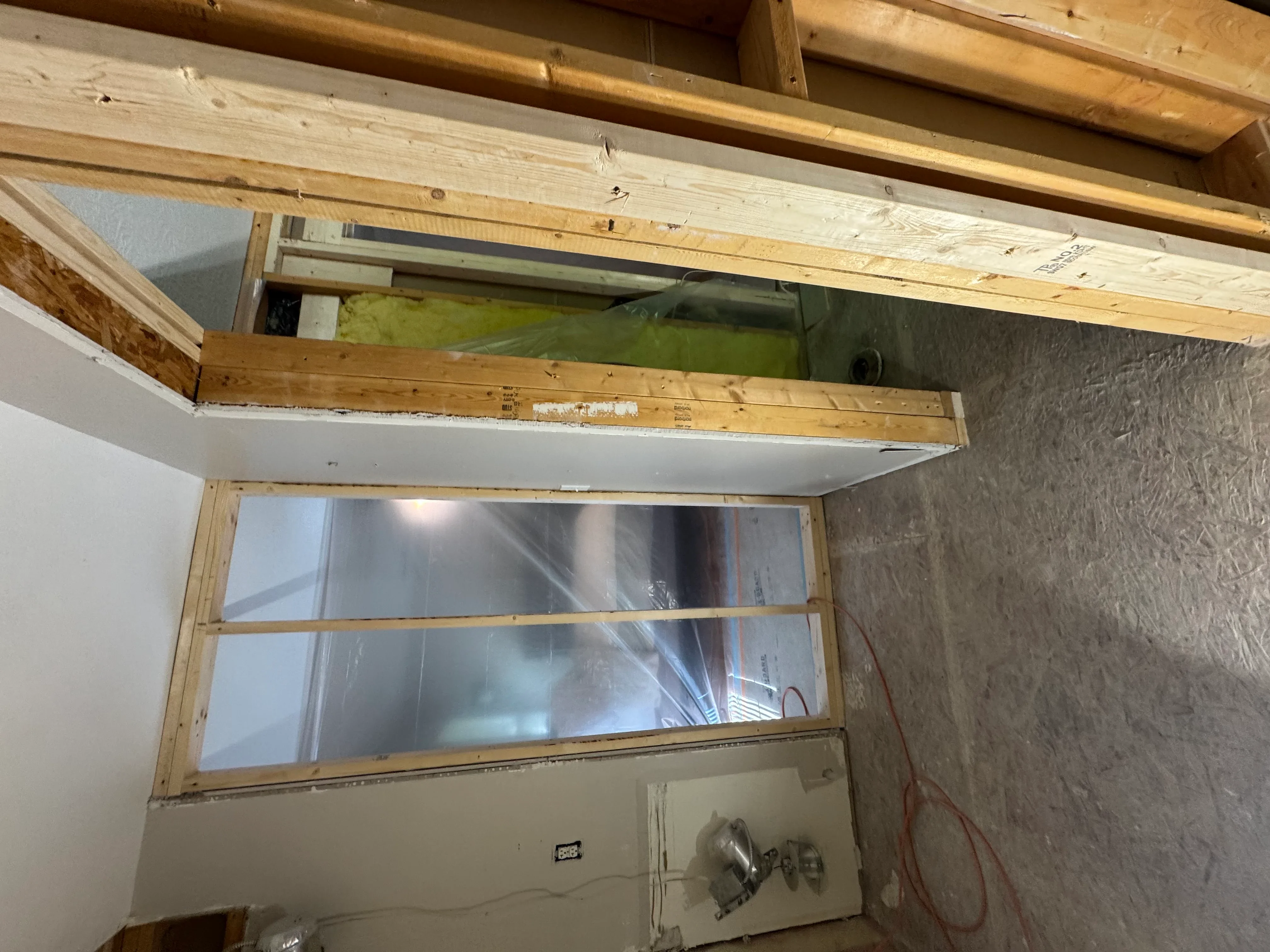 Interior window with three glass panes in wooden frame during installation, exposed framing and drywall