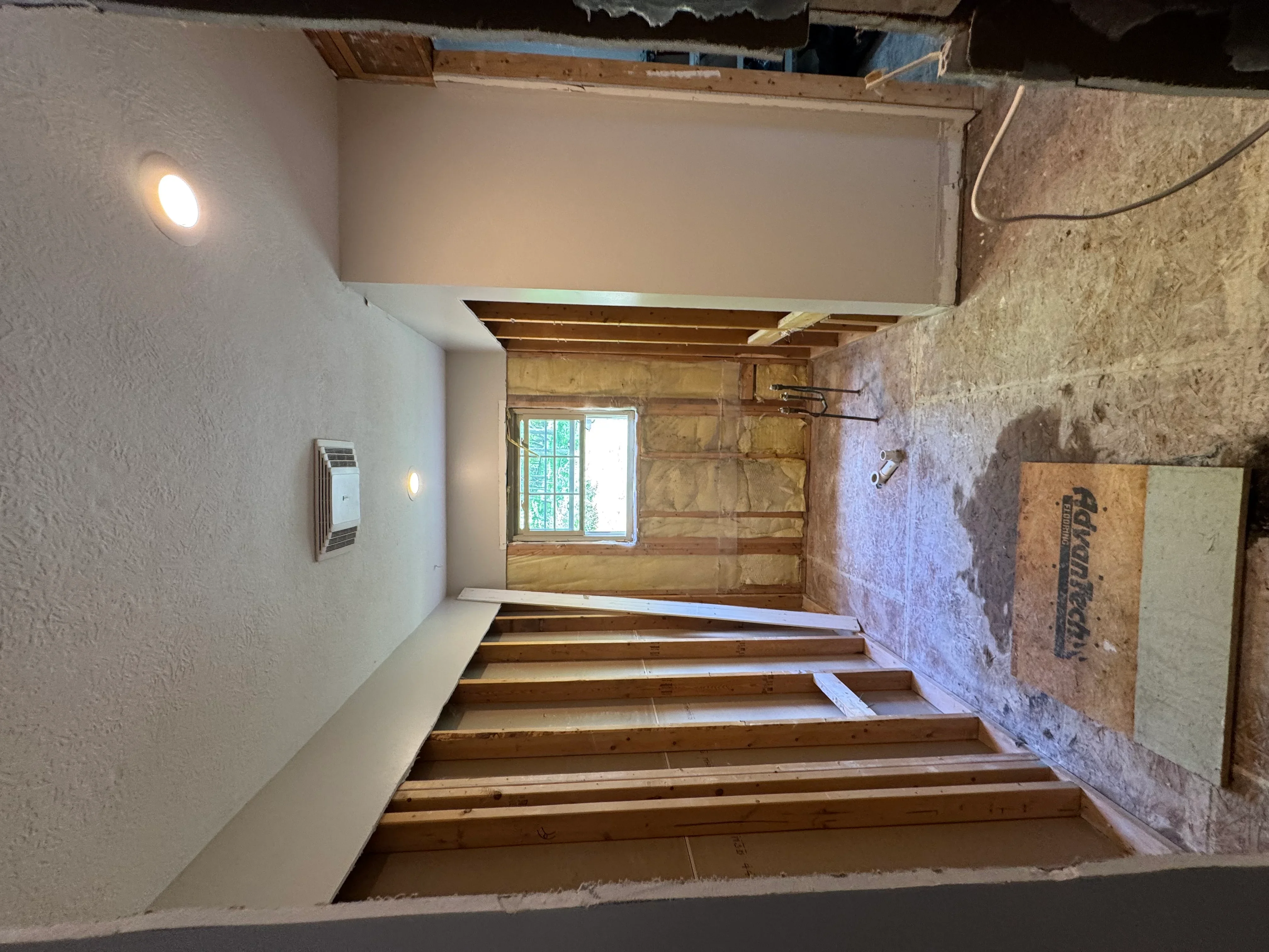 Interior renovation with drywall walls, wooden floor joists, and window framing