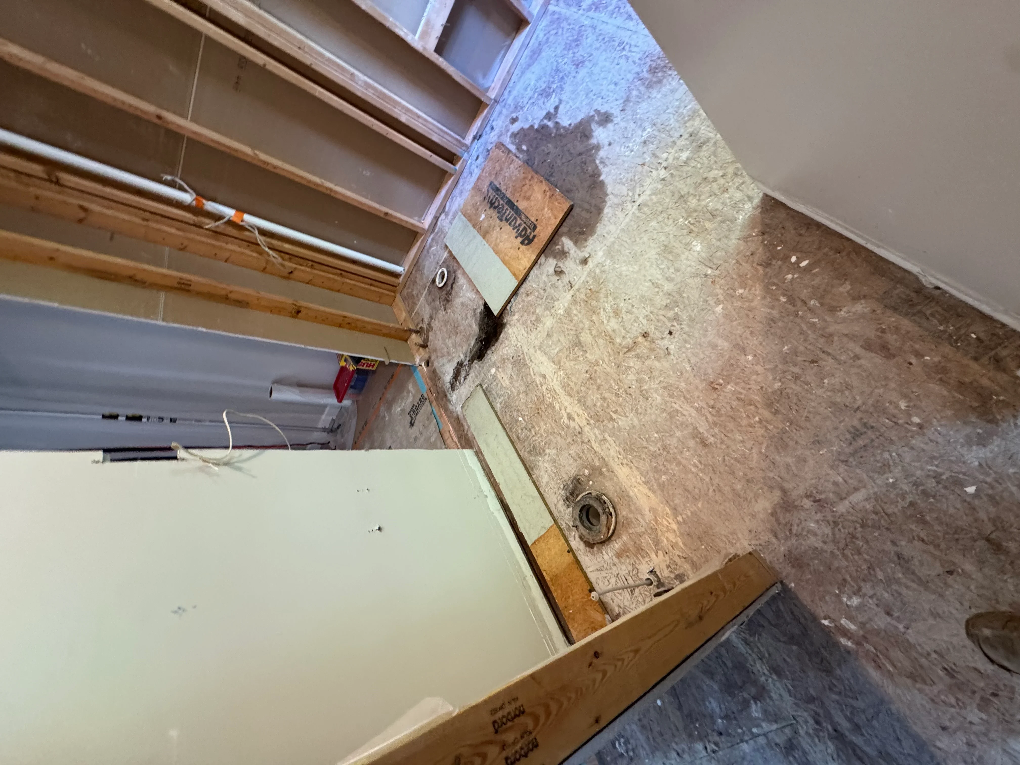 Interior demolition showing exposed OSB subfloor, concrete substrate, and stripped wall surfaces during renovation prep