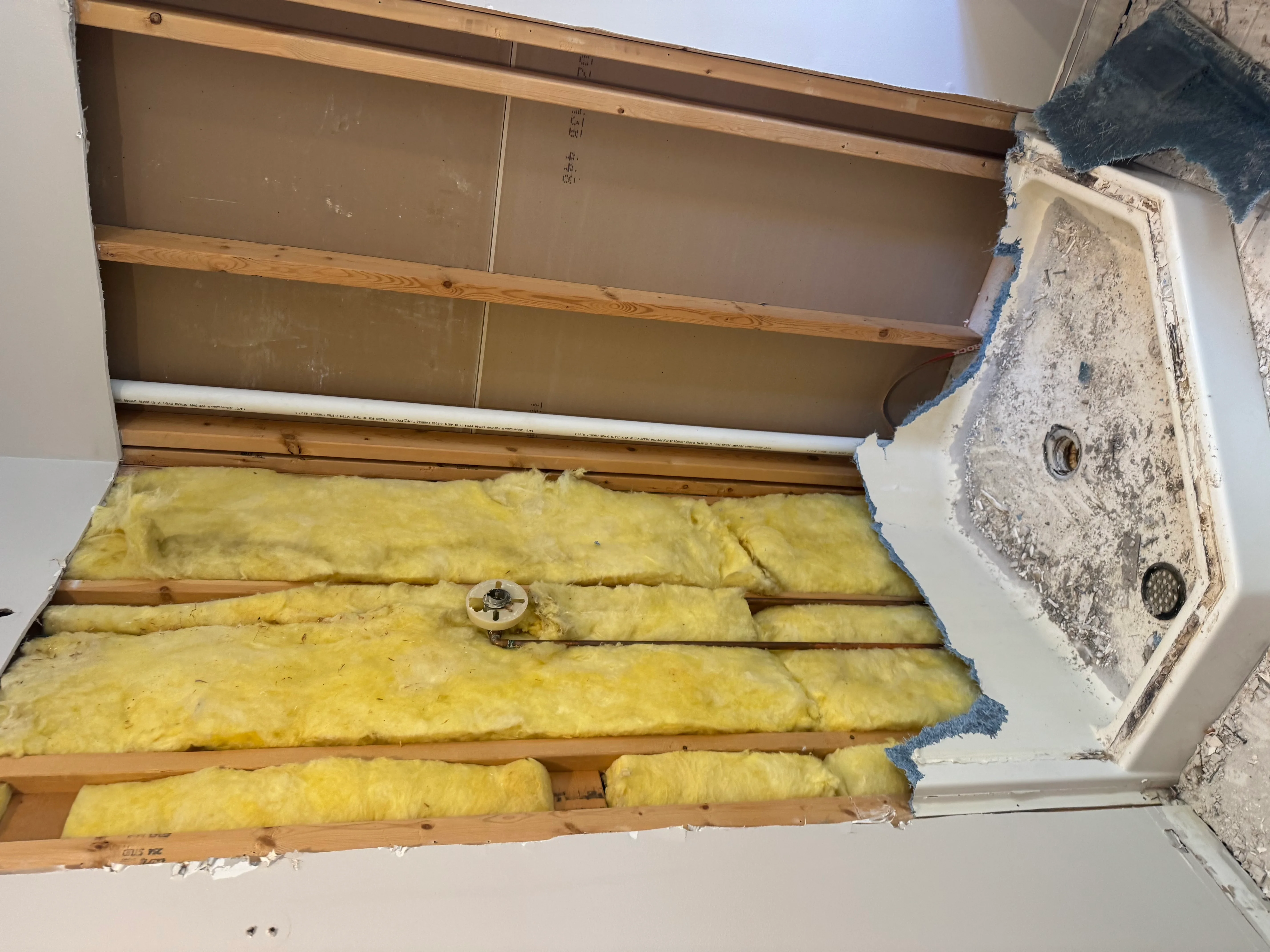 Yellow fiberglass insulation batts between wooden joists with drywall panels staged overhead