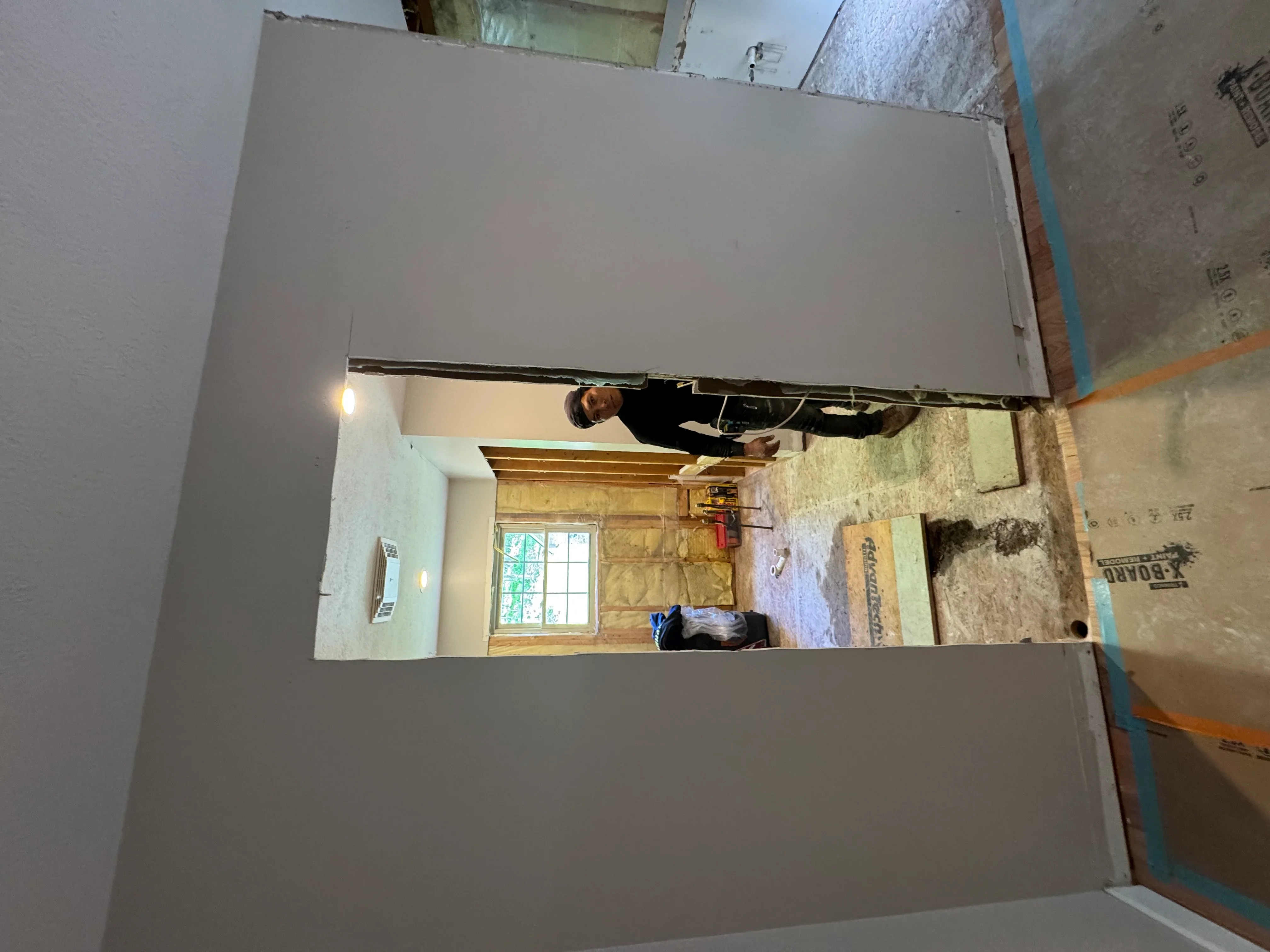 Drywall installation on walls and ceiling with exposed insulation and framing in renovation project